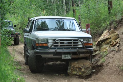 1996 Ford Bronco - A white Ford Bronco navigates a rocky trail, with a Jeep following behind on a wooded path.