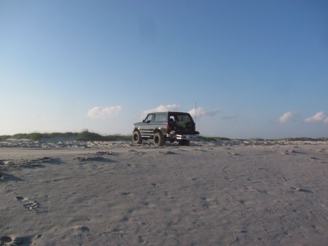 1995 Ford Bronco - A 1995 Ford Bronco is parked on a sandy beach, with dunes and a clear blue sky in the background.