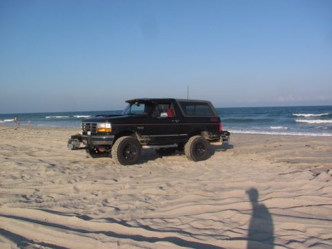 1995 Ford Bronco - A black 1995 Ford Bronco sits on the sand near the ocean waves.