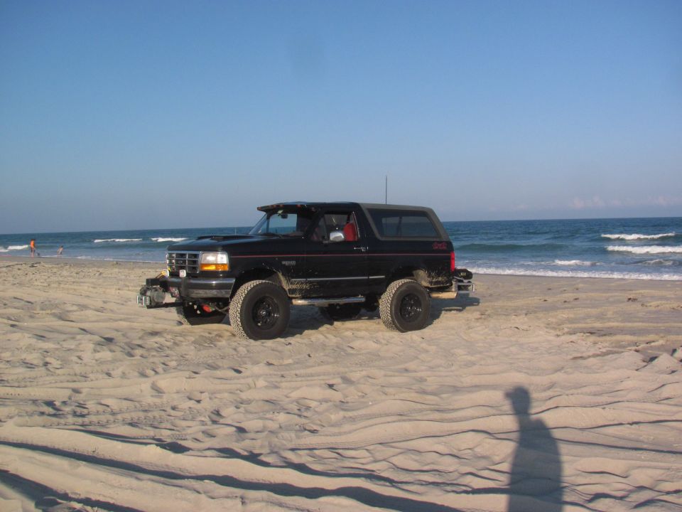 Black 1995 Ford Bronco parked on a sandy beach with the ocean in the background