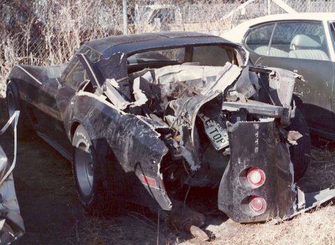 1976 Chevrolet Corvette - The rear of a severely damaged black 1976 Chevrolet Corvette is shown, with debris and crumpled metal obscuring much of the vehicle.