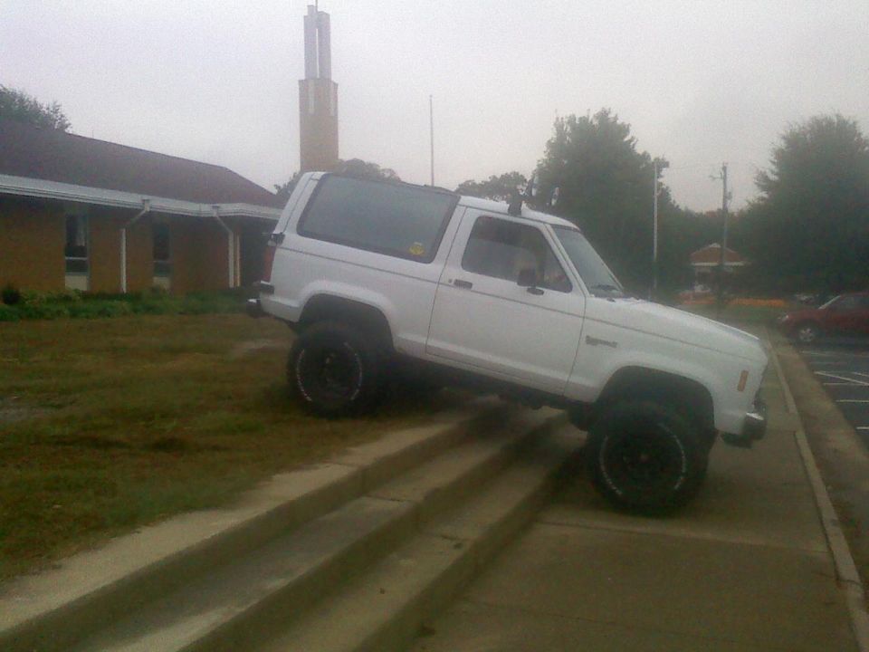 White 1988 Ford Bronco II driving up concrete stairs next to a building