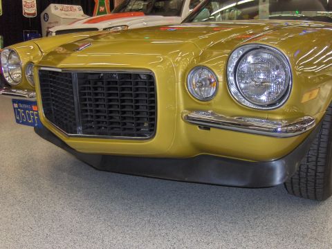 1979 Chevrolet Camaro - Front view of a gold 1970s Chevrolet Camaro, its distinctive grille and headlights. Another vehicle is visible behind it.