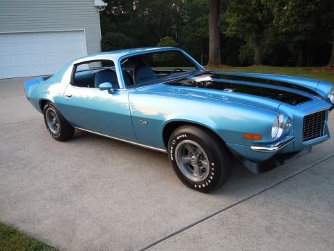 1972 Chevrolet Camaro - A light blue Chevrolet Camaro with black stripes on the hood is parked in front of a garage.