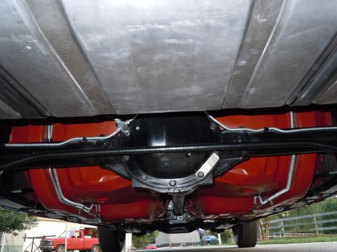 1972 Chevrolet Camaro - The underside of a vehicle reveals its fuel tank and differential, with a red pickup truck in the background.