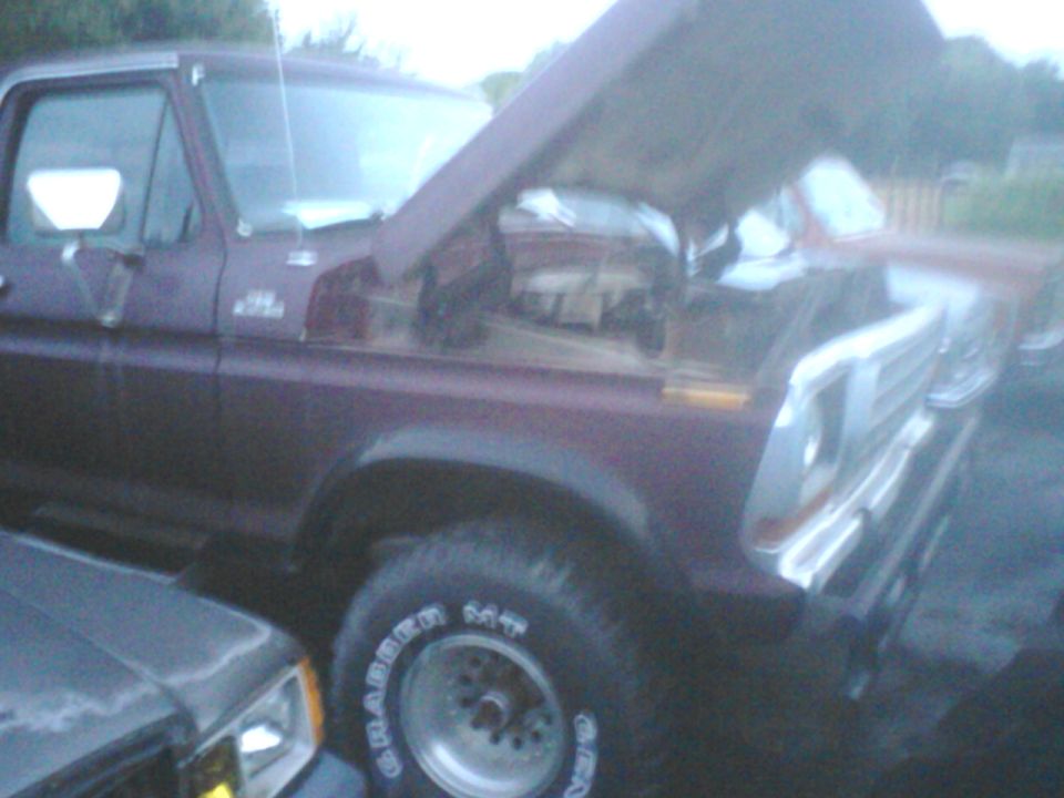 Maroon Ford truck with hood open, showing engine. Another vehicle is partially visible to the left