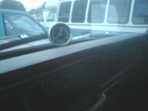 1988 Ford Bronco - A gauge is mounted on the hood of a dark-colored vehicle, with other vehicles and an RV in the background.