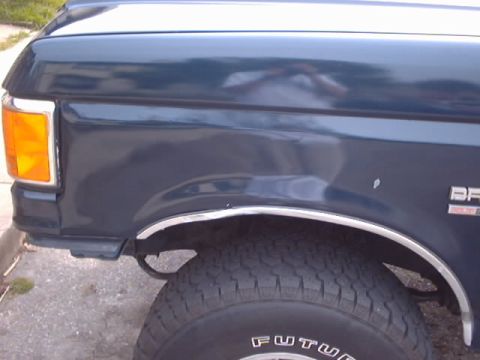 1990 Ford Bronco - The side view shows the fender, wheel, and tire of a dark blue Ford Bronco.