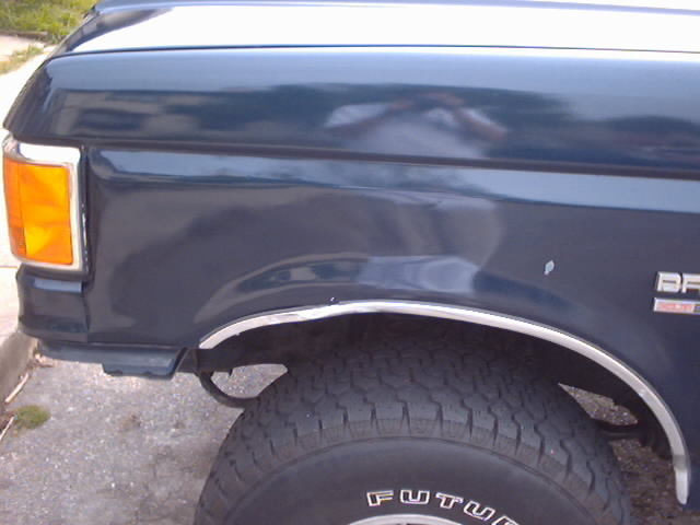 Close-up of a dark blue 1990 Ford Bronco's front fender, wheel well, and tire