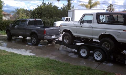 1978 Ford Bronco - A 1978 Ford Bronco is loaded onto a trailer, towed by a pickup truck. Another truck is visible in the background.