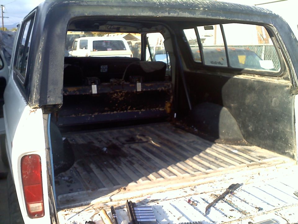 Back of an old SUV with a black roof and interior cargo area. Another white SUV is visible in the background