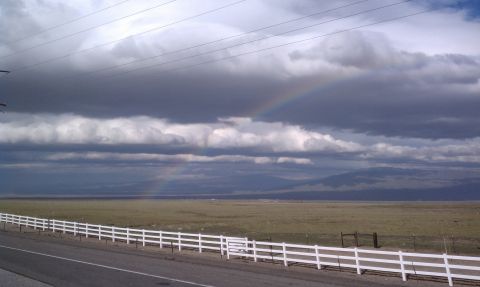 1978 Ford Bronco - A rainbow appears through dark clouds over a rural landscape with a white fence along the road.