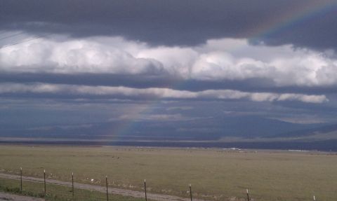 1978 Ford Bronco - A dramatic sky with dark clouds and a hint of a rainbow looms over a vast, open field.