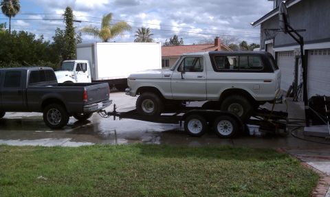 1978 Ford Bronco - A white 1978 Ford Bronco is transported on a trailer towed by a dark-colored pickup truck.