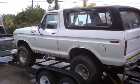 1978 Ford Bronco - Passenger-side view of a white full-size Ford Bronco with a black removable hardtop, loaded on a black tandem-axle car hauler trailer in a…