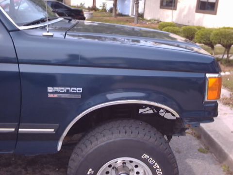 1990 Ford Bronco - A close-up view of the front fender and wheel of a dark blue 1990 Ford Bronco.