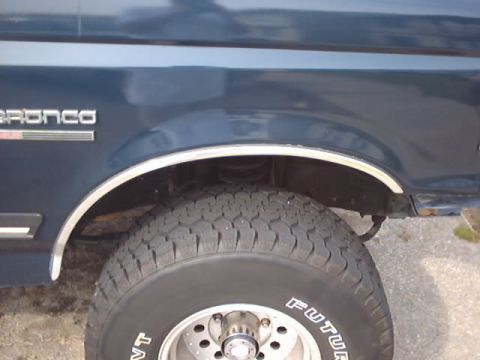 1990 Ford Bronco - Close-up of the side of a dark blue SUV, showing the fender, wheel well, and tire. The "BRONCO" badge is visible.