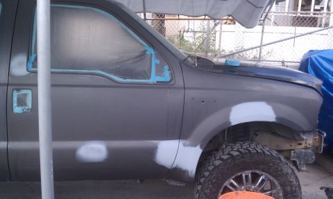 1978 Ford Bronco - Side view of a Ford Super Duty pickup mid-bodywork, its cab and front fender in dark gray primer with white body-filler spots sanded in and…