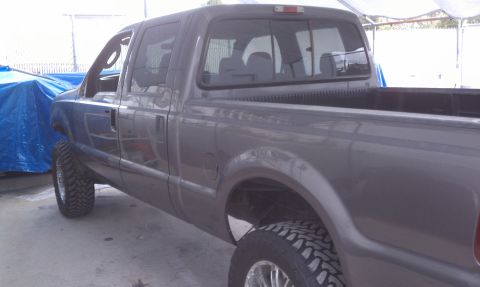 1978 Ford Bronco - Gray pickup truck with lifted suspension and off-road tires is parked next to a blue tarp.