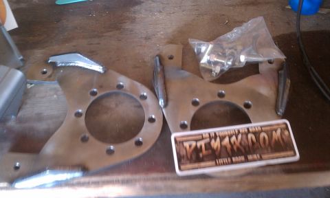 1978 Ford Bronco - Pair of brake caliper brackets and a bag of hardware are laid out on a wooden surface.