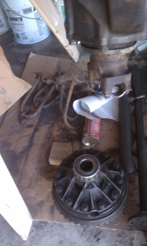 1978 Ford Bronco - A differential carrier sits on cardboard, surrounded by various automotive parts and a spray can.