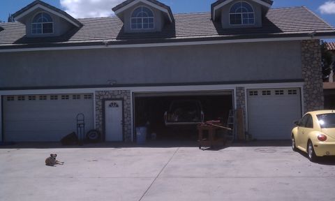 1978 Ford Bronco - A yellow Volkswagen Beetle is parked in front of a garage, with another vehicle visible inside one of the bays.