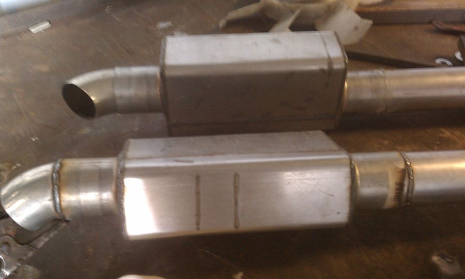 Two stainless steel performance mufflers lying on a workbench