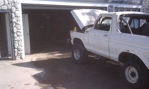 1978 Ford Bronco - The vehicle is a white SUV with its hood up, parked in front of an open garage door. A roll cage is visible inside.