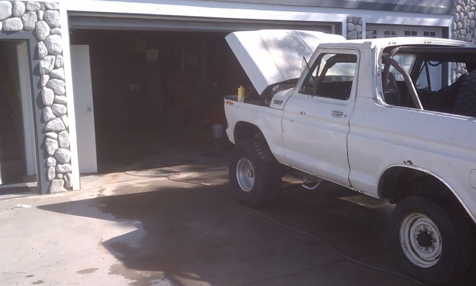 white SUV with hood open, parked in front of garage. Roll cage visible inside