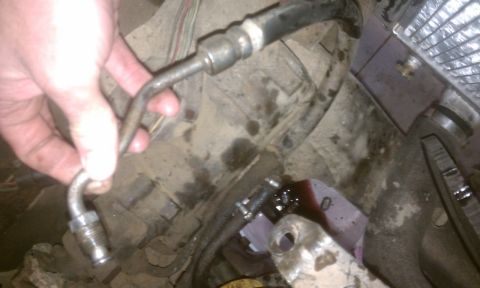 1978 Ford Bronco - A hand holds a metal tube over dirty engine parts, with a small spill of red fluid visible.