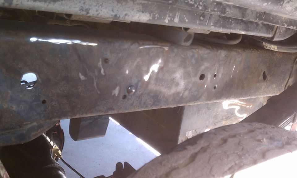 Rusty vehicle frame with holes and welds, viewed from below
