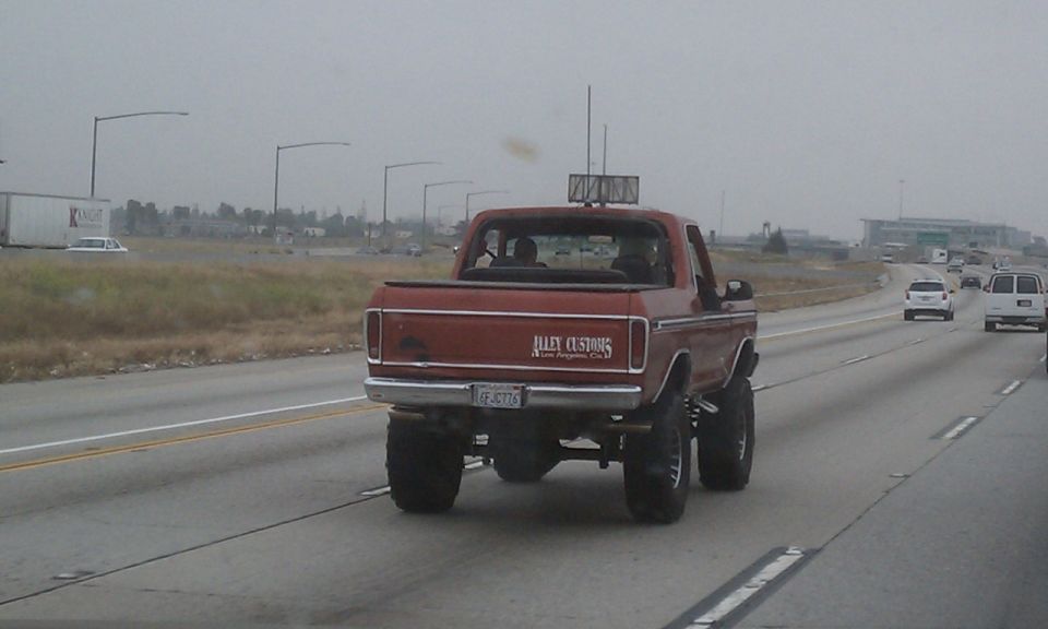 Lifted red topless Ford Bronco on the freeway with Alley Customs tailgate decal