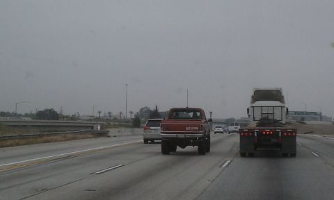 1978 Ford Bronco - A red pickup truck drives on the highway, its rear end and lifted suspension clearly visible.