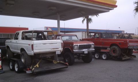 1978 Ford Bronco - Three trucks are parked at a gas station. The white Bronco on the left is on a trailer.