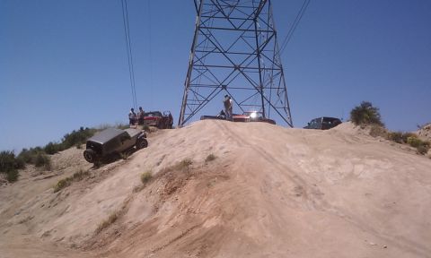 1978 Ford Bronco - Several off-road vehicles navigate a steep, sandy incline under a large power line tower on a sunny day.