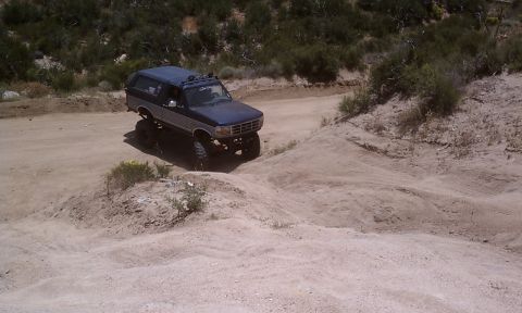 1978 Ford Bronco - This lifted SUV navigates a dusty trail, its two-tone paint and prominent grille suggesting a model from the early to mid-1990s.