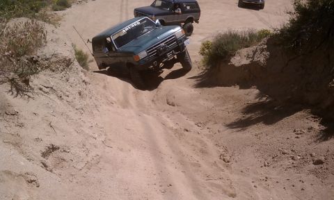1978 Ford Bronco - Two SUVs tackle a challenging off-road course on a sunny day.