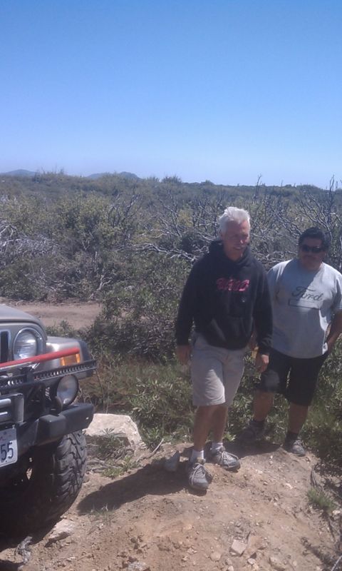 1978 Ford Bronco - Two men stand next to a Jeep Wrangler on a dirt trail, with brush and hills in the background.