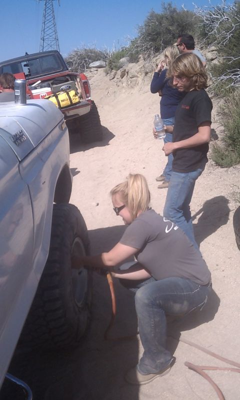 1978 Ford Bronco - A group of people are gathered around a 1978 Ford Bronco, with one person airing up the tire during an off-road excursion.
