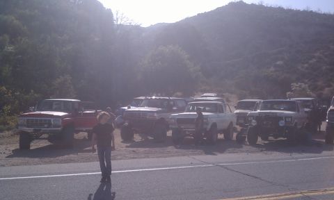 1978 Ford Bronco - A group of off-road vehicles are gathered on the side of a road in a mountainous area.