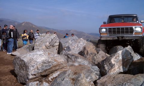 1978 Ford Bronco - A red pickup truck navigates a rocky terrain with spectators watching.
