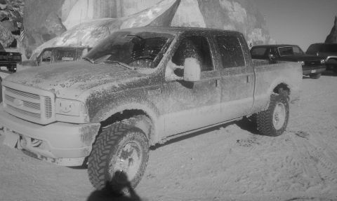 1978 Ford Bronco - High-contrast black-and-white three-quarter front view of a mud-splattered Ford Super Duty crew cab pickup on mud-terrain tires, parked on…
