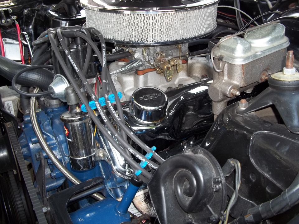 Close-up of a V8 engine bay, showing carburetor, distributor, spark plug wires, and brake master cylinder