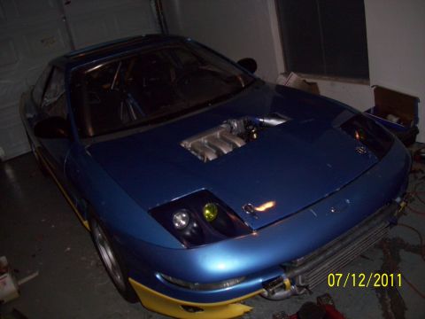 1995 Ford Probe - Modified 1995 Ford Probe with custom hood scoop revealing engine components and yellow lower body trim.