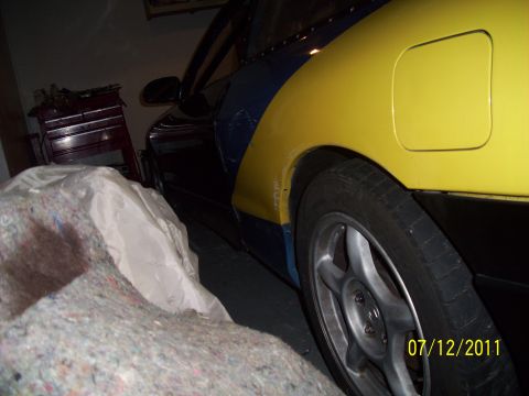 1995 Ford Probe - A car with a two-tone blue and yellow paint scheme is partially covered by a blanket in a garage.