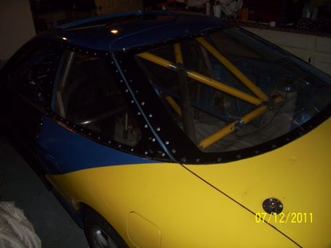 1995 Ford Probe - A modified car with a roll cage is seen from the rear, painted in yellow and blue.