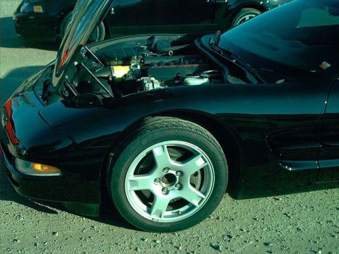 2000 Ford Crown Victoria - Front quarter view of a black sports car with its hood open, revealing the engine bay. A second vehicle is partially visible in the backgro…