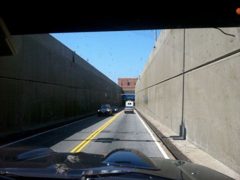 1995 Ford Bronco - A view from inside a vehicle shows two cars and a white RV traveling down a road flanked by tall concrete walls.