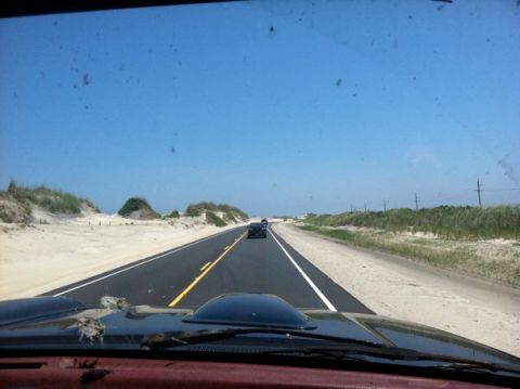 1995 Ford Bronco - Driving on a coastal road with sand dunes and other cars ahead under a clear blue sky.