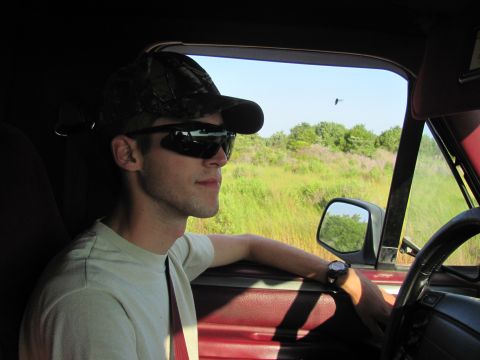 1995 Ford Bronco - Man driving a vehicle with a red interior, looking out the window at a grassy field.